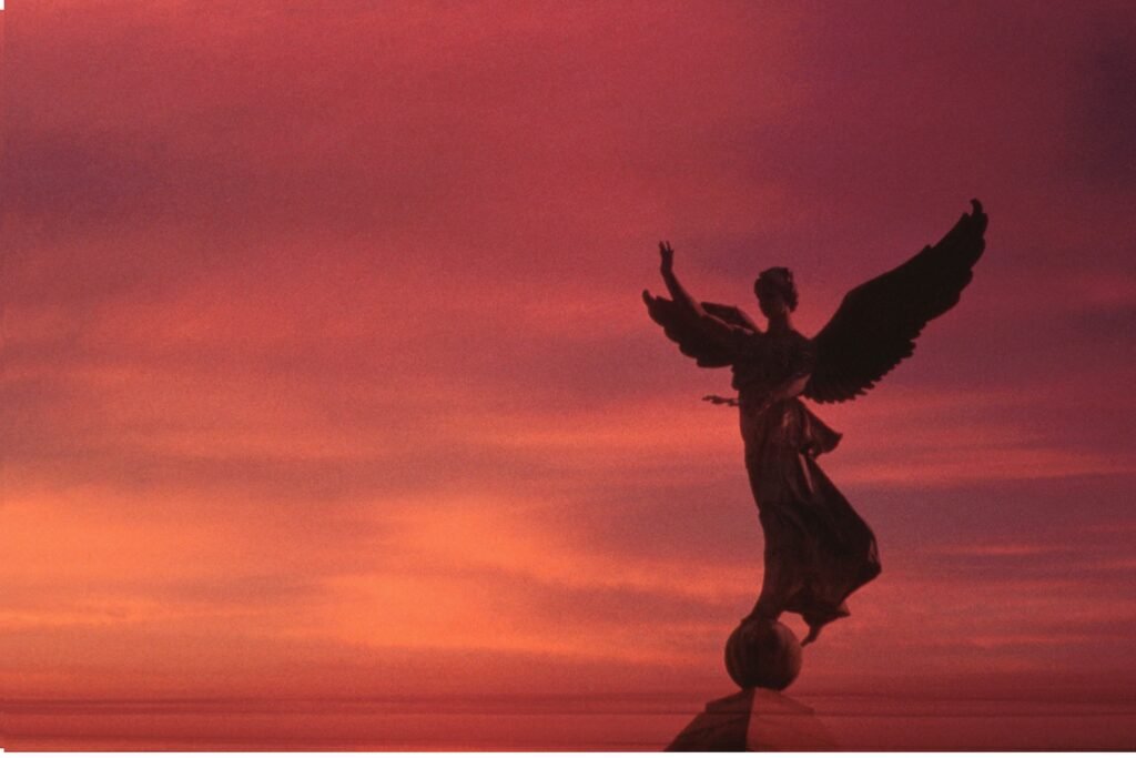 Estátua de um anjo com fundo alaranjado.